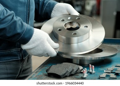 Brake disc in the hands of a mechanic close-up. On the desktop is a set of brake pads.Spare parts of the car suspension. Repair and maintenance of the car in the service center.