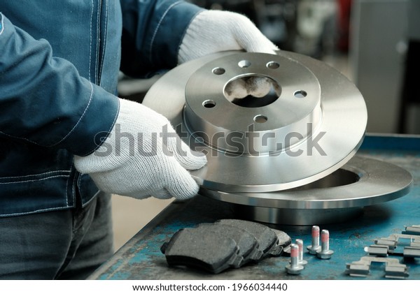 Brake disc\
in the hands of a mechanic close-up. On the desktop is a set of\
brake pads.Spare parts of the car suspension. Repair and\
maintenance of the car in the service\
center.