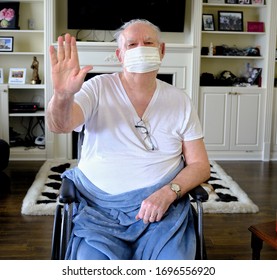 BRAMPTON, ONTARIO / CANADA - APRIL 7, 2020: Senior Male Sitting In Wheelchair Wearing Medical Mask And Holding Hand Up In Stop Or Stay Away From Me Message