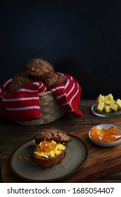 A Bran Muffin With Grated Cheese And Apricot Jam Sits On A Stoneware Plate.  A Small Plate Of Apricot Jam And Butter Sits In The Background.  Red And White Striped Cloth Lines A Basket Full Of Muffins