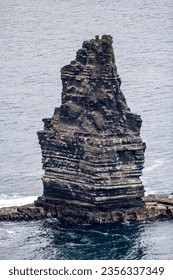 Branaunmore sea stack on Cliffs of Moher, surrounded by calm waters of sea and in background, enormous height, linear irregular rock texture, cloudy day in County Clare in Ireland. Wild Atlantic Way