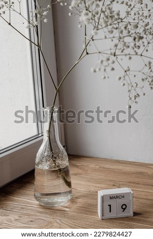 A branch of gypsophila in a bottle vase. Perpetual calendar and the date March 19 on it