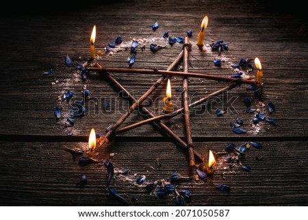 Branch Pentagram - witchcraft tools of natural wood. Wooden pentagram with candles, small stones and petals of delphinium. Occultism and mysticism.