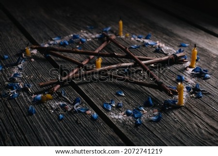 Branch Pentagram - witchcraft tools of natural wood. Wooden pentagram with candles in circle of salt and blue petals. Occultism and mysticism.