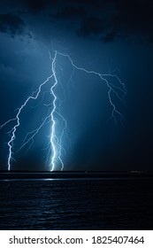 Branched Lightning Bolts Strike Down To The Surface Of The Water At Night