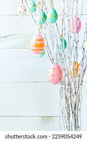 The branches of the trees decorated with multi-colored Easter eggs stand in a vase on a white wooden background. Easter tree. Easter composition.