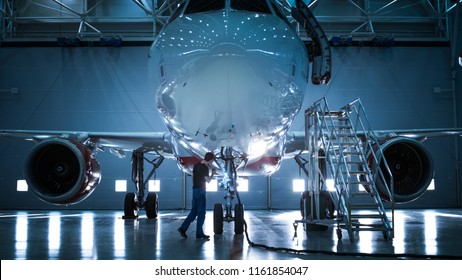 Brand New Airplane Standing in a Aircraft Maintenance Hangar while Aircraft Maintenance Engineer/ Technician/ Mechanic goes inside Cabin via Ladder/ Ramp.