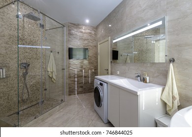 Brand New Bathroom Interior Design. Luxury Modern Bathroom With White Bath Tub, Washing Machine, Walk In Shower With Glass Door.