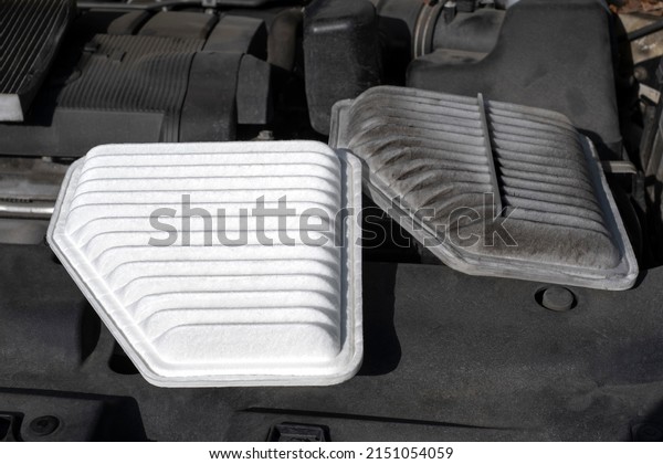 A brand new\
clean engine filter placed next to the old dirty used filter for\
comparison under the car\
hood.