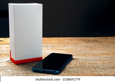 A Brand New Smartphone Next To A Blank Box On Wooden Table