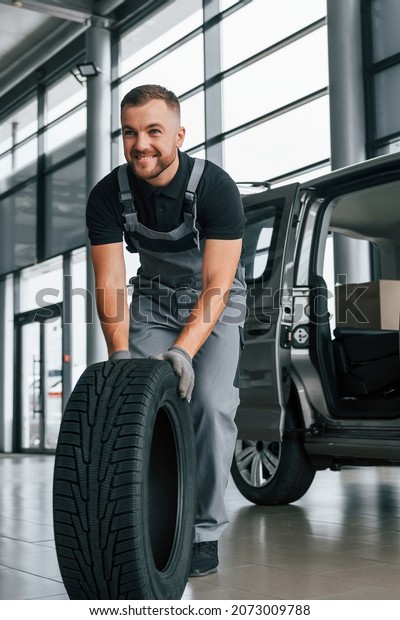 Brand new tire. Man in uniform is working in the\
autosalon at daytime.