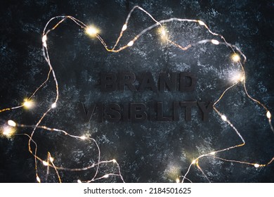Brand Visibility text barely visible on dark background with fairy lights around it, concept of businesses struggling to become popular