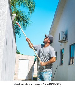 Brasilia, Federal District - Brazil. April, 21, 2021. Painter man passing a wall putty ( in portuguese: Textura de parede ) on an external wall of a residence with a beautiful blue sky in composition.