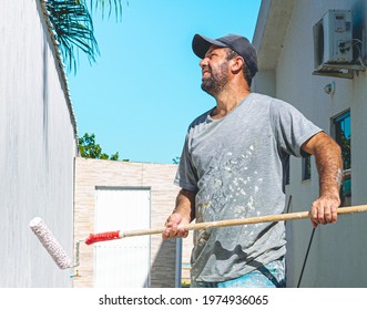 Brasilia, Federal District - Brazil. April, 21, 2021. Painter man passing a wall putty ( in portuguese: Textura de parede ) on an external wall of a residence with a beautiful blue sky in composition.