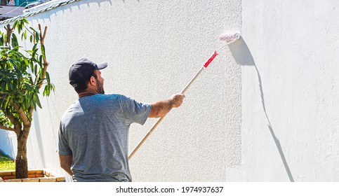 Brasilia, Federal District - Brazil. April, 21, 2021. Painter man passing a wall putty ( in portuguese: Textura de parede ) on an external wall of a residence .