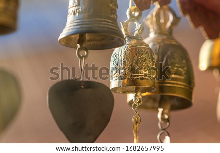 ฺSmall brass bells hanging on temple roof, close up shinning beautiful brass bells. Faith of Buddhism in Thailand. Soft warm Light beam in the air. Selected focus, blur background and foreground.