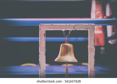 Brass Boxing Bell Suspended On Metal Frame With Blurry Fighting Ring In Background