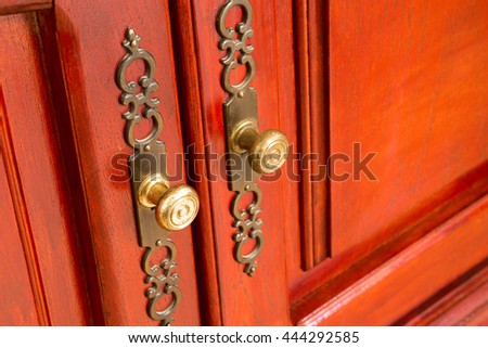 Brass door handles with ornate escutcheons on a wooden cabinet or cupboard with raised panels, close up oblique angle view with copy space