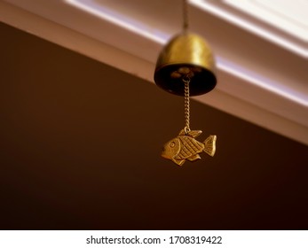 Brass fish chime hanging by a chain under a bell on blurred white and brown wall background - Shutterstock ID 1708319422