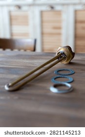 Brass heating element rests on wooden surface. Red cap tops the metallic tube. Three gaskets sit nearby - two blue, one silver. Tools lie still, unattended, on rustic wood. Ideal for plumbing, heating