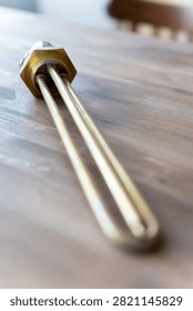 Brass heating element rests on wooden surface. Red cap seals electrical connection point. Simple industrial design for water or liquid heating. Ideal for plumbing, heating, or boiler system visuals