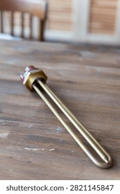 Brass heating element rests on wooden surface. Red cap seals electrical connection point. Simple industrial design for water or liquid heating. Ideal for plumbing, heating, or boiler system visuals