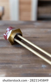Brass heating element rests on wooden surface. Red cap seals electrical connection point. Simple industrial design for water or liquid heating. Ideal for plumbing, heating, or boiler system visuals