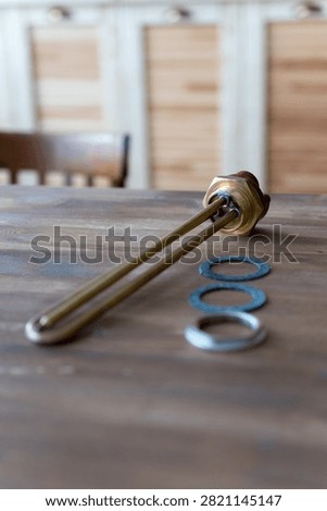 Brass heating element rests on wooden surface. Red cap tops the metallic tube. Three gaskets sit nearby - two blue, one silver. Tools lie still, unattended, on rustic wood. Ideal for plumbing, heating