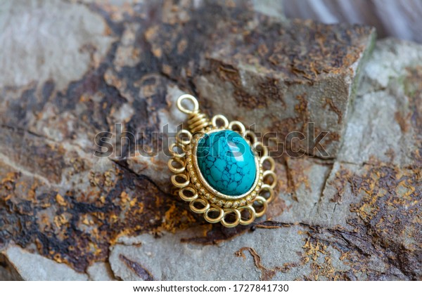 Brass pendant with natural turquoise gemstone\
on rocky background