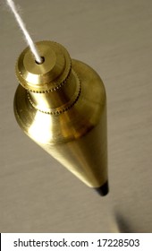 Brass plumb bob hanging over metallic surface