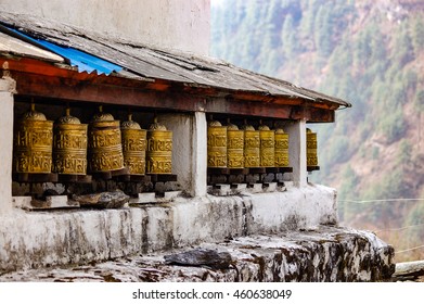 The brass prayer wheels  lined up under the wooden roof in a village on the Everest base camp trekking route in Himalayas on a foggy day.
