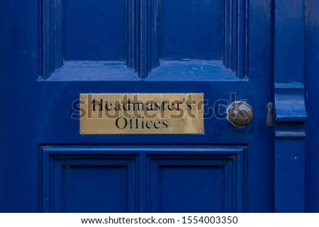 A brass sign reading Headmasters offices on a old blue door with a brass handle