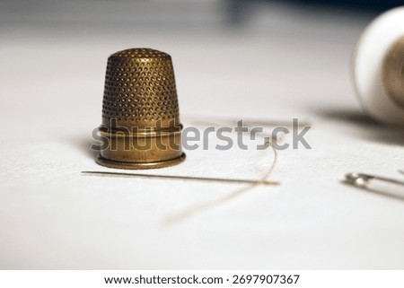 A brass thimble next to different sorts of needles
