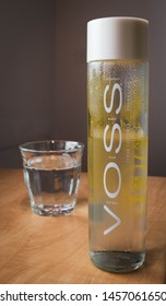 Bratislava, Slovakia - Jul 21, 2019: Voss Cooled Norway Water Bottle With A Flavor Of The Lemon And Cucumber On The Table With A Full Glass Of Healthy Water