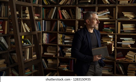 brave 45 years old men with gray hair and beard standing with book, shelves with books on background - Shutterstock ID 1283150935