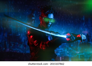 A Brave Cyberpunk Warrior Fights With A Sword In His Hands Against The Backdrop Of The Night Rainy City Of The Future. Game, Virtual Reality.