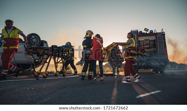 Brave Firefighter Carries Injured Young Girl to\
Safety where She Reunited with Her Loving Mother. In the Background\
Car Crash Traffic Accident Courageous Paramedics and Firemen Save\
Lives