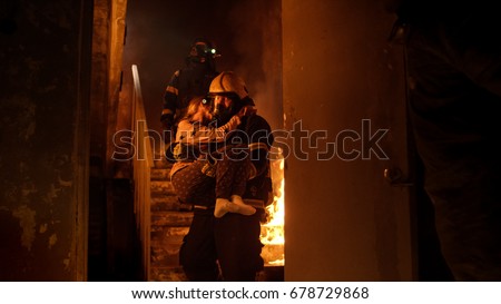 Brave Fireman Descends Stairs of a Burning Building with a Saved Girl in His Arms.