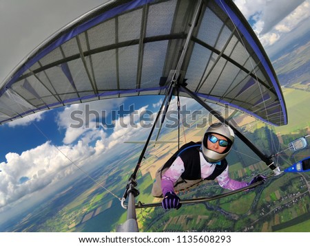 Brave girl hang glider pilot fly high above ground on a colorful purple hang glider. Wide angle action camera shot