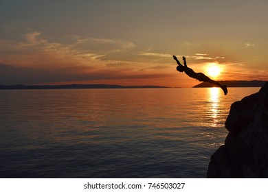 brave guy jumps from a cliff into the sea with a beautiful sunset