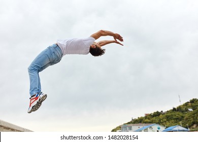 Brave Guy In White T-shirt And Jeans Bending His Back, Stunt Performer Enjoying His Work In The Street, Full Length Side View Photo