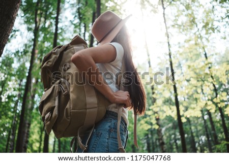 Brave hipster girl traveling alone and looking around in forest on outdoors wearing treveler backpack and hold location map in hand