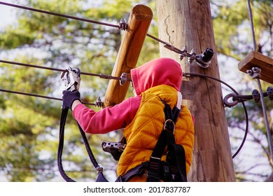 Brave Kid In A High Wire Park Above The Ground. Ziplining. The Child Passes The Rope Obstacle Course. Back View