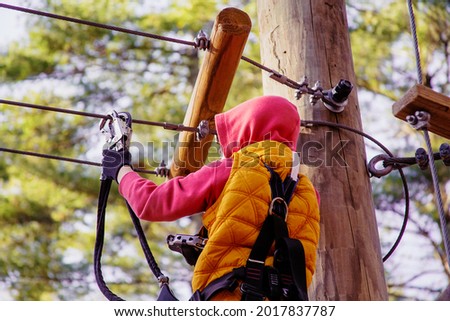 Brave kid in a high wire park above the ground. Ziplining. The child passes the rope obstacle course. back view