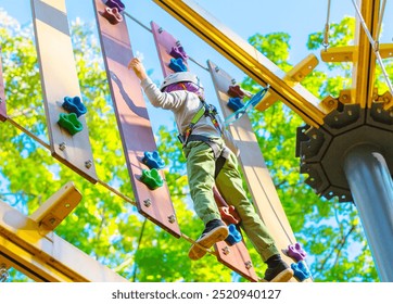 brave little boy in helmet and fastened to safety rope climbing at adventure park in autumn season. Work out concept - Powered by Shutterstock