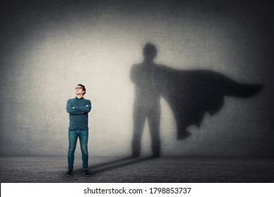 Brave man keeps arms crossed, looks confident, casting a superhero with cape shadow on the wall. Ambition and business success concept. Leadership hero power, motivation and inner strength symbol. - Shutterstock ID 1798853737