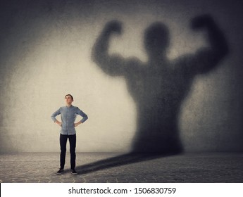 Brave teenager boy facing his fears as a powerful hero. Guy casting a strong muscular bodybuilder shadow, showing big biceps. Self defense, inner strength and motivation and confidence concept.