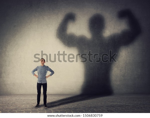 Brave teenager boy facing his fears as a\
powerful hero. Guy casting a strong muscular bodybuilder shadow,\
showing big biceps. Self defense, inner strength and motivation and\
confidence concept.