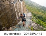 Brave woman hiker climbs up a narrow trail along a waterfall at the edge of a cliff, in Glacier National Park at Grinnell Glacier Trail