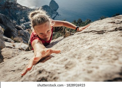 Brave young woman climber fearlessly climbs up sheer stone wall in mountains, overcoming obstacles. Dangerous chasm balancing, adrenaline and courage in extreme sports. - Shutterstock ID 1828926923